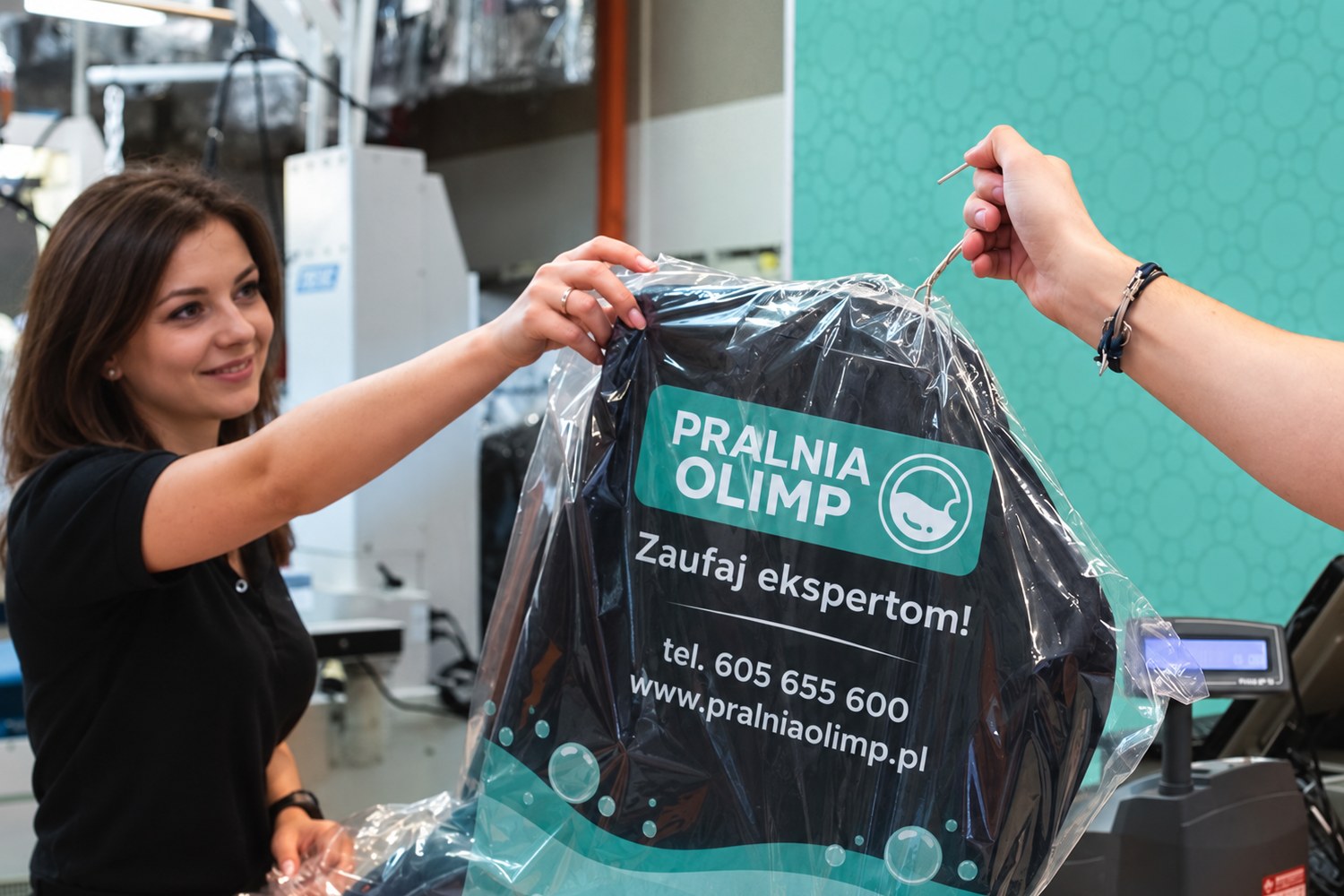 Pracownica Pralni Olimp wydaje klientowi odzież w firmowej folii